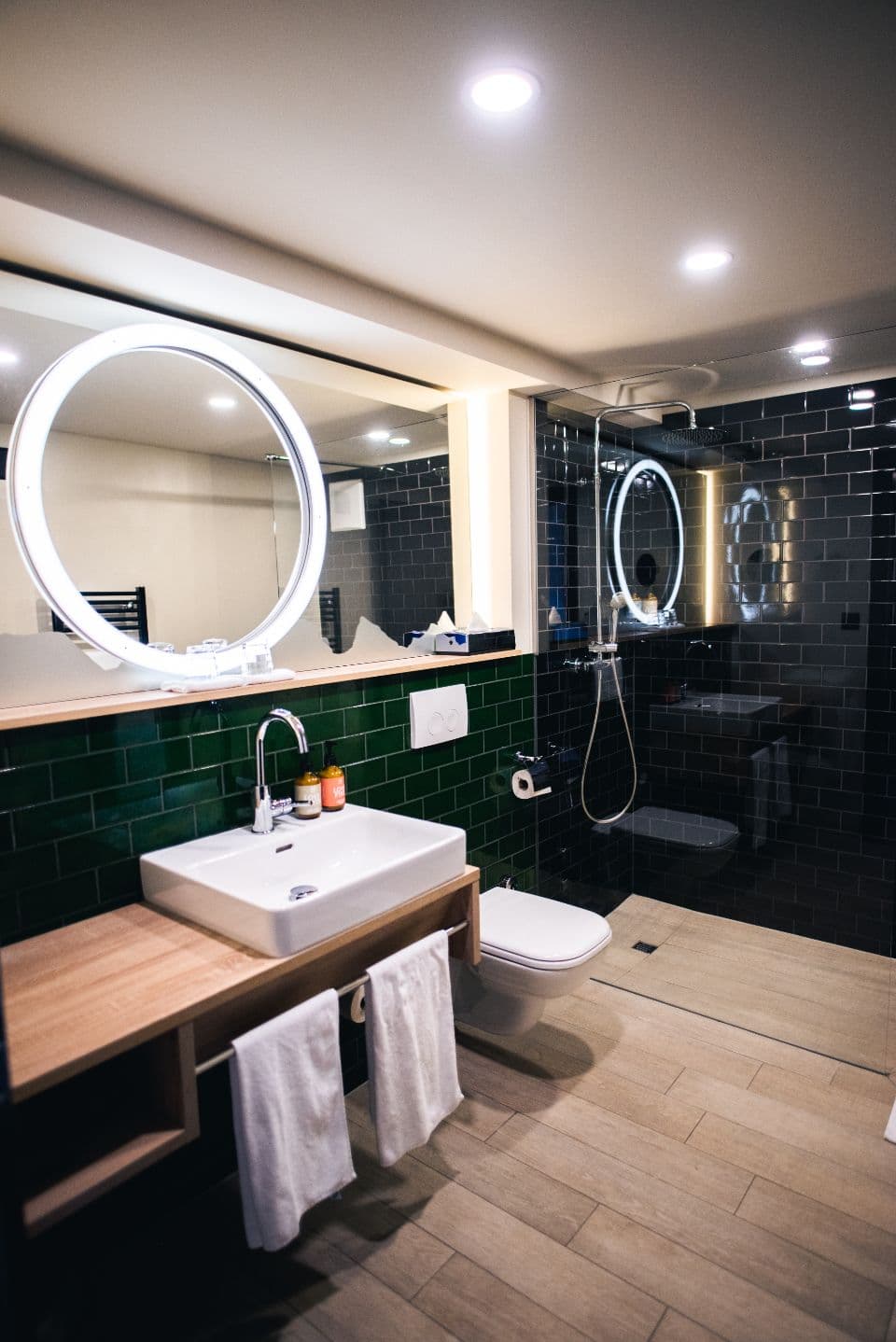 A modern bathroom with a lit mirror and dark tiles